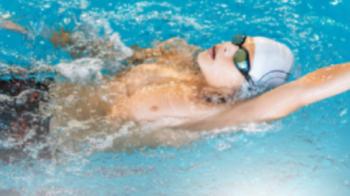 Junger Schwimmer mit Schwimmkappe und Schwimmbrille schwimmt Rückenschwimmen in einem klaren, blauen Schwimmbecken