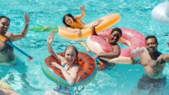 Mehrere fröhliche Menschen in einem Pool mit bunten Schwimmringen, sie winken und genießen das Wasser
