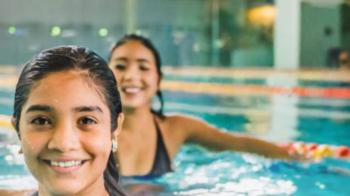 Zwei Mädchen stehen im Schwimmbecken und lächeln fröhlich in die Kamera